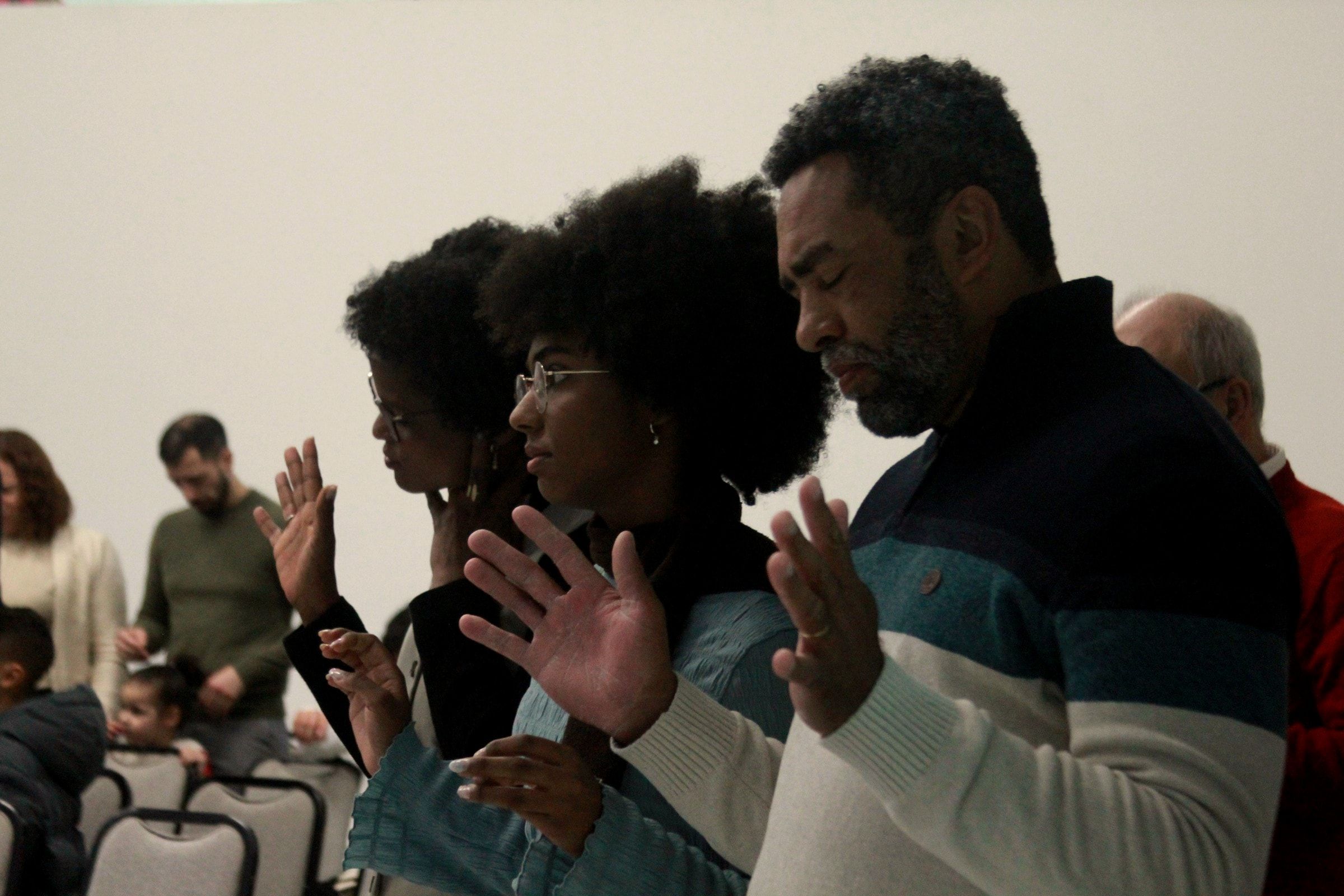 Uma família a orar de mãos erguidas durante o culto